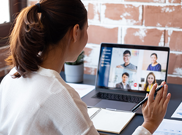 Egy személy az íróasztalánál ül, és laptopján keresztül egy öt résztvevős videókonferencián vesz részt – tipikus iroda- vagy home office jelenet.